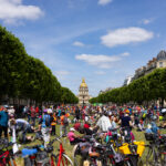 Vue des pelouses de Breteuil lors du pique-nique, sous le soleil, avec des cyclistes au premier plan et le dôme des Invalides en arrière-plan